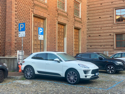 Porsche Macan parked on cobblestone street in Italy with parking signs and brick facade building