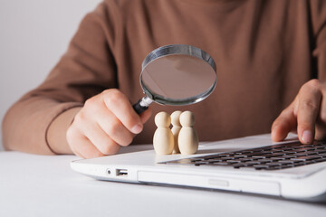 Fototapeta premium Businessman looking through a magnifying glass at wooden figures on a laptop