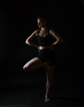 Sportliche Frau in dynamischer Pose vor dunklem Hintergrund. Kraft, Balance, Fitness, K&ouml;rperkontrolle und mentale St&auml;rke in einer modernen Sport- und Lifestyleaufnahme.