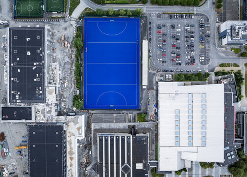 Aerial view of the UCD Sports Centre featuring a vibrant blue synthetic pitch, modern campus buildings, and a parking area in Dublin, County Dublin, Ireland.