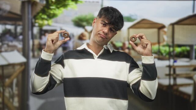 Man holds two biscuits between thumb and forefinger with a skeptical face on a street market; taste test uncertainty.