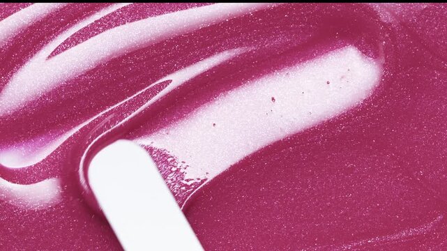 Close up of white spatula playing with pink shimmering lip gloss texture, satisfying make up lipgloss stroke. Cosmetic product swatch background