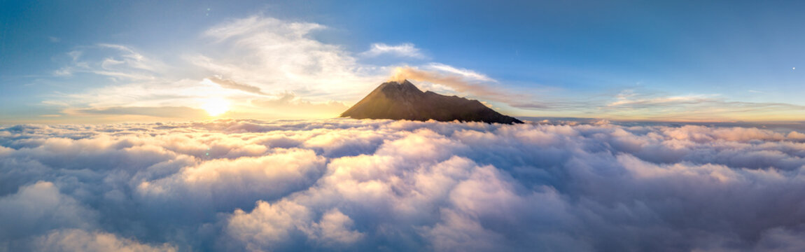 Aerial view of Mount Merapi volcano rising above a thick layer of white clouds during a golden sunrise in Cangkringan, Daerah Istimewa Yogya, Indonesia.