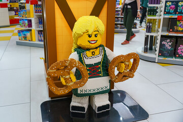 Naklejka premium Munich, Germany - May 31, 2026: LEGO figure in Bavarian costume holding giant pretzels inside a Munich store. Concept of local culture, tourism and creative design