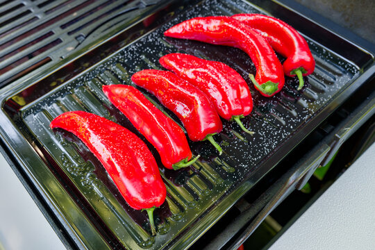 A high-angle close-up shot of a modern gas grill filled with salted and oiled red romano peppers on a black sheet on a gas grill being grilled for a vegetarian meal.