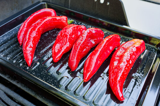 A high-angle close-up shot of a modern gas grill filled with salted and oiled red romano peppers on a black sheet on a gas grill being grilled for a vegetarian meal.