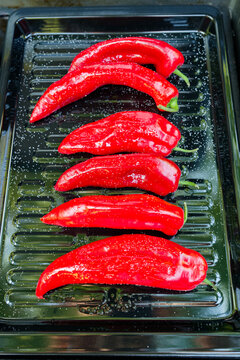 A high-angle close-up shot of a modern gas grill filled with salted and oiled red romano peppers on a black sheet on a gas grill being grilled for a vegetarian meal.