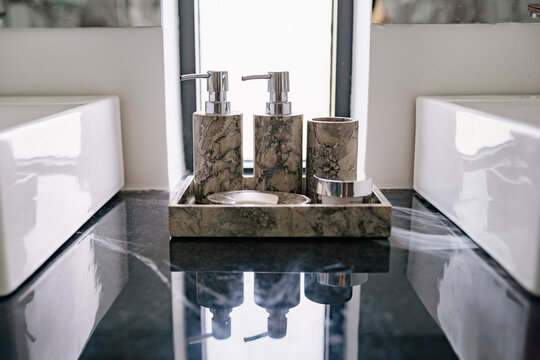 Elegant marble soap dispensers and coordinated bathroom accessories arranged neatly on a sleek reflective countertop in a bright and modern bathroom setting during the day