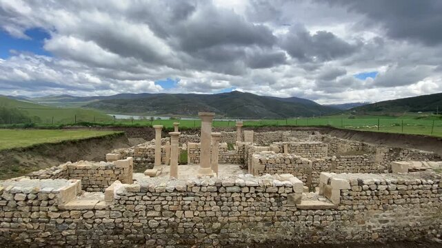 Ancient ruins of Satala Ancient City in Kelkit, G&uuml;m&uuml;şhane, T&uuml;rkiye. Historic Roman archaeological site featuring stone foundations and columns set against a dramatic cloudy sky and lush green landscap