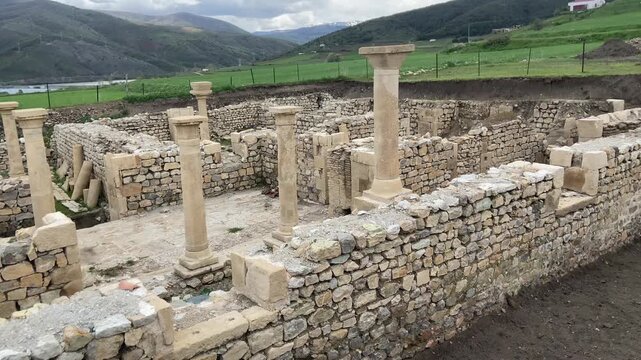 Ancient ruins of Satala Ancient City in Kelkit, G&uuml;m&uuml;şhane, T&uuml;rkiye. Historic Roman archaeological site featuring stone foundations and columns set against a dramatic cloudy sky and lush green landscap