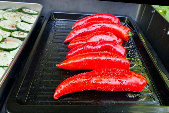 A high-angle close-up shot of a modern gas grill filled with salted and oiled red romano peppers on a black sheet on a gas grill being grilled for a vegetarian meal. 