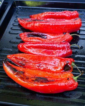 Fresh red pointed peppers and seasoned zucchini slices are cooking on a barbecue grill. A close-up of a gas grill loaded with fresh vegetables.