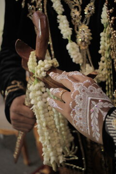 Javanese wedding couple in black velvet attire, groom holding a traditional keris with jasmine.
