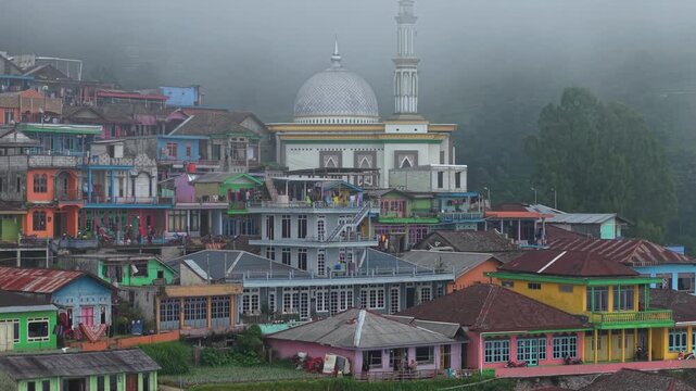 Aerial view of Nepal Van Java village with colorful houses and a mosque dome nestled on a misty hillside in Kecamatan Kaliangkrik, Jawa Tengah, Indonesia.