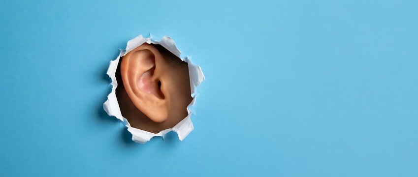 Human ear peeking through torn paper on bright blue background, concept of listening, eavesdropping, information gathering and privacy concerns, studio shot.