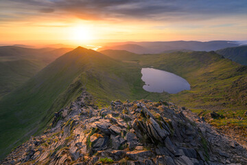 Fototapeta premium Golden sunrise seen from Helvellyn overlooking spectacular view of Swirral Edge, Red Tarn and Ullswater in The Lake District mountains.