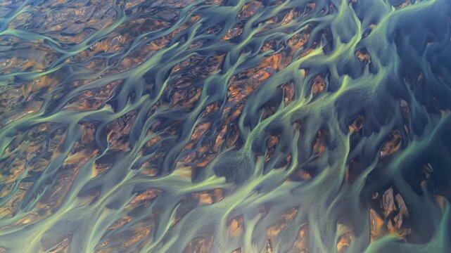Aerial view of intricate braided glacial rivers flowing through dark volcanic sand with greenish water patterns in Hella, Rangarthing ytra, Iceland.
