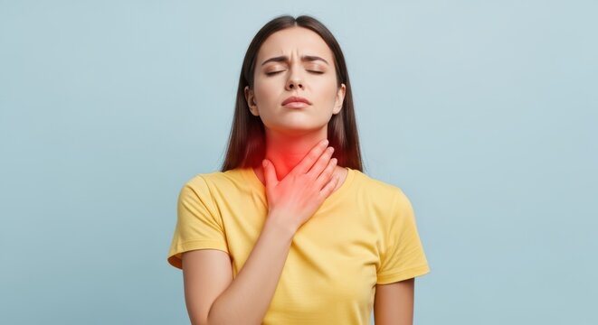 Young woman with sore throat touching her neck, feeling pain and discomfort, isolated on blue background