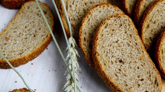 Freshly sliced whole grain bread arranged on a white cloth with stalks of wheat positioned alongside, showcasing the texture and color of the bread and natural elements