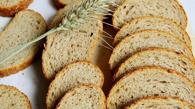 Slices of whole grain bread arranged on a white surface with a stalk of wheat placed artistically among the bread, showcasing texture and natural elements in a kitchen setting