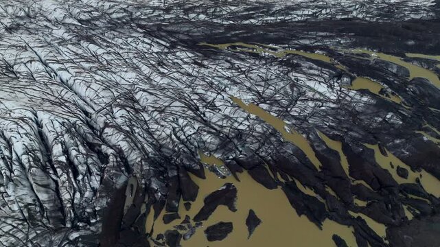 Aerial view of the textured glacier ice covered in volcanic ash with brown meltwater pools at Jokulsarlon, Sveitarfelagid Hornaf, Iceland.
