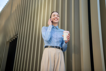 Fototapeta premium Young businesswoman talking phone enjoying coffee break outside