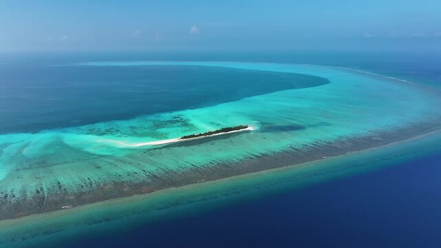 Aerial view of a narrow tropical island with lush vegetation surrounded by turquoise coral reefs and deep blue ocean waters in Fulhadhoo, Baa Atoll, Maldives.