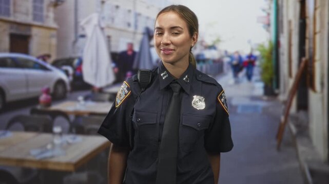 Woman police officer displays badge and makes call sign with her hand while smiling at a street cafe scene; friendly reassurance.