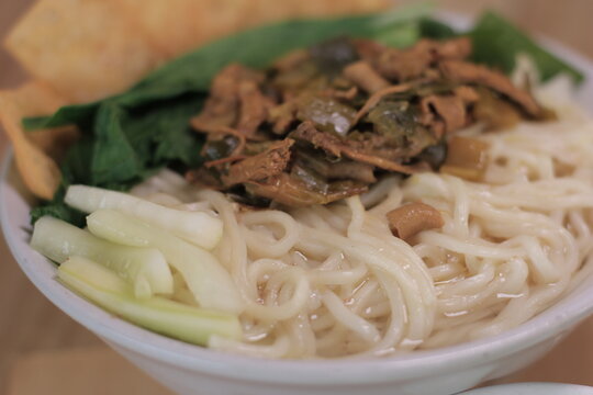 A bowl of Indonesian chicken noodles or mie ayam served with chopsticks, crackers, and scallions.