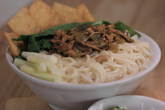 A bowl of Indonesian chicken noodles or mie ayam served with chopsticks, crackers, and scallions.