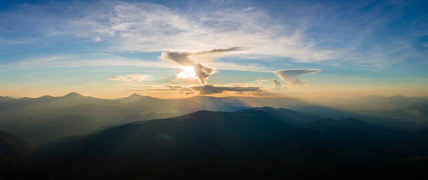 Aerial view of dark mountain hills with bright sunrays of setting sun at sunset. Hazy peaks and misty valleys in evening