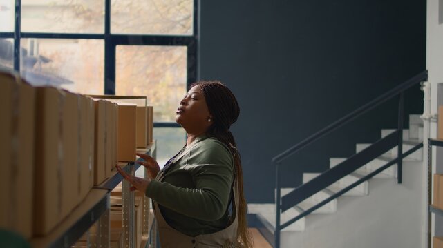 Head of logistics in warehouse handling cardboard boxes full of products ready to be shipped to clients. Meticulous supervisor in distribution center placing parcels on cabinet shelves