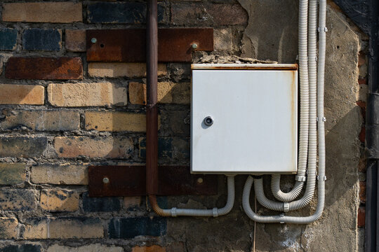 Electrical Junction Box Installed on an Aged Brick Wall Surrounded by Conduits and Metal Fixtures, Showcasing Urban Infrastructure and Maintenance Details