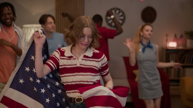 Medium slowmo portrait of Caucasian young adult woman dancing with USA flag, celebrating Independence Day with multiethnic friends at home. Clip is perfect for holiday marketing campaigns