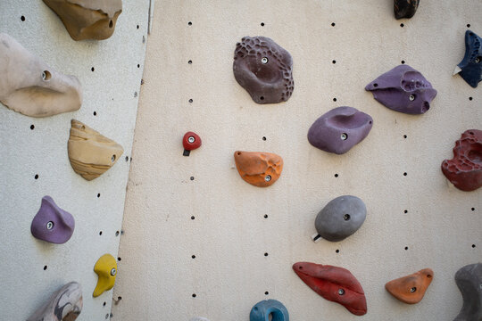 Colorful climbing holds on a beige indoor climbing wall, bouldering gym background