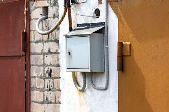 A Weathered Electrical Box Mounted on a Wall with Various Cables and Pipes in an Urban Setting, Highlighting Industrial Design and Textures