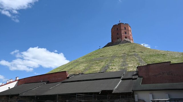 Gediminas' Tower, a Historic Landmark of Vilnius, Lithuania, Stands Tall on a Green Hill Against a Clear Blue Sky with Fluffy White Clouds on a Sunny Day.