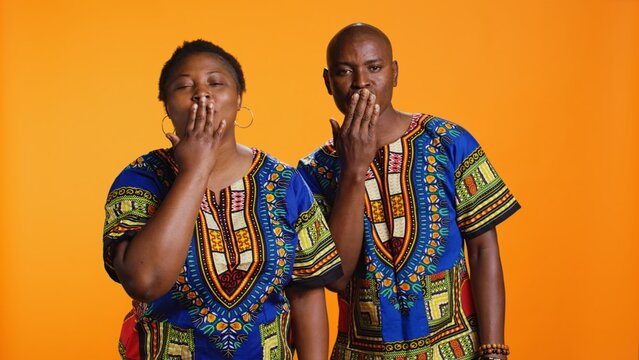 Sweet african american couple sending air kisses on camera, presenting flirty gesture and showing their affection. Ethnic man and woman blowing kiss in studio, traditional clothing items.