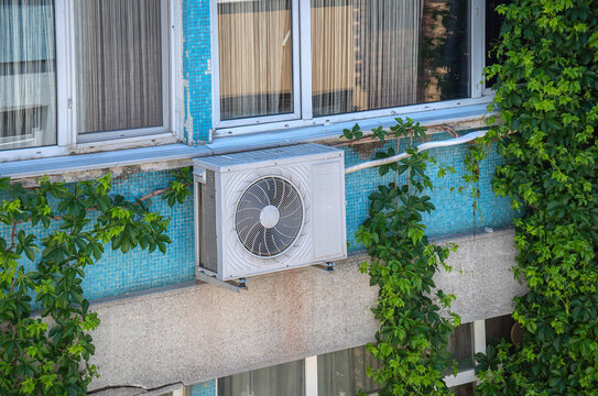 The air conditioner's outdoor unit is on the exterior of the apartment building. Ivy plants covering the exterior of the building.