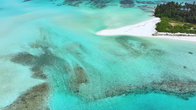 Aerial view of the turquoise lagoon and pristine white sand beach with lush green vegetation and coral reefs in Fulhadhoo, Baa Atoll, Maldives.