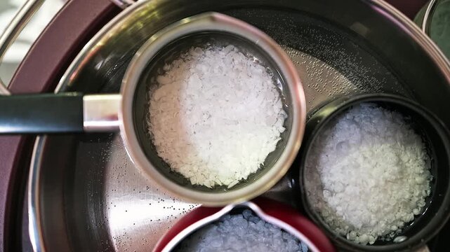 Melting white candle wax flakes in a metal container over a boiling water bath on a stove burner.