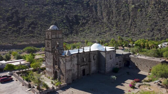 View the historic San Javier Mission in Baja California Sur Mexico surrounded by palm trees at sunrise near Loreto