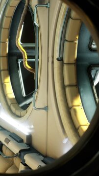 The scene shows a circular window looking into a hallway. The walls are smooth and curved. Glowing lights are visible along the path. The setting appears modern and is likely inside a building.