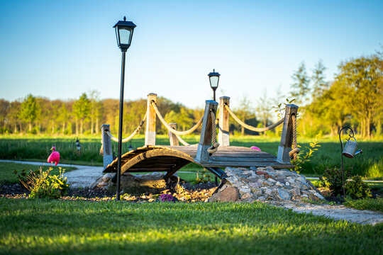 Die tiefstehende Sonne malte lange Schatten ins Gras, die Laternen wachten wie stille W&auml;chter &uuml;ber den Garten, und die Holzplanken schienen Geschichten von Reisenden zu erz&auml;hlen, die hier f&uuml;r einen Mo