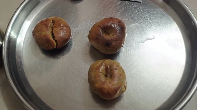 Three traditional baked wheat flour baati on a stainless steel plate top view