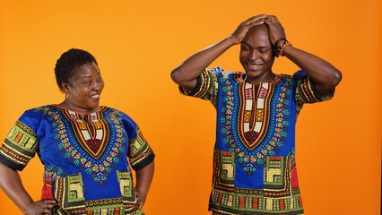 Obraz premium Joyful man and woman laughing together in studio, having fun with silly jokes over orange background. African american people enjoying funny moments with laugh, amused couple.