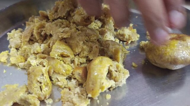 Crushing roasted baati with hand and pouring hot dal curry on a steel plate close up