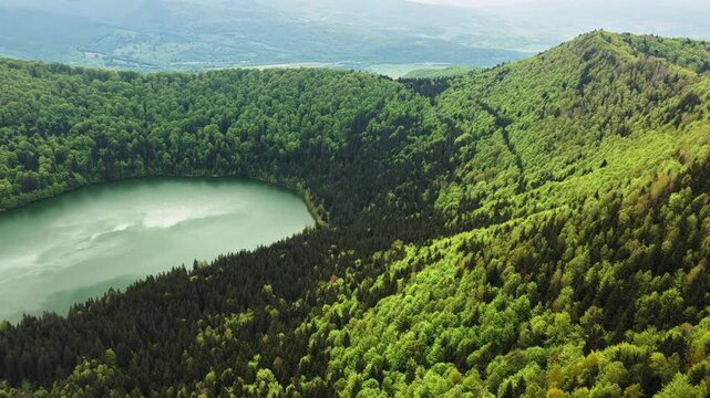 Aerial drone view at low altitude of a lakeside meadow with timber logs by a crater lake, Lacul Sfanta Ana, Harghita, Romania.