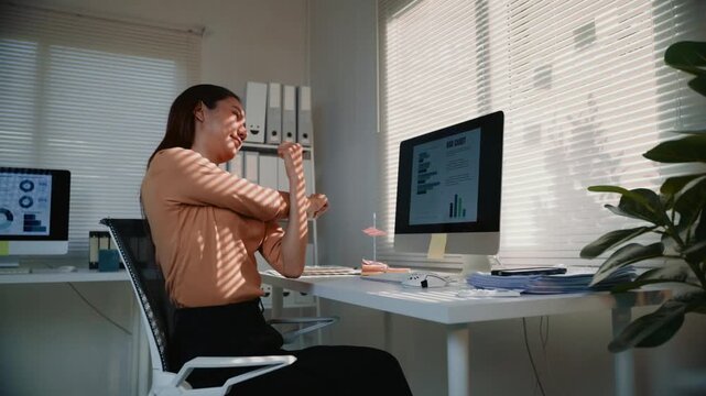Asian businesswoman feeling tired and taking a break from computer work. Female employee relaxing and stretching her arms at the desk