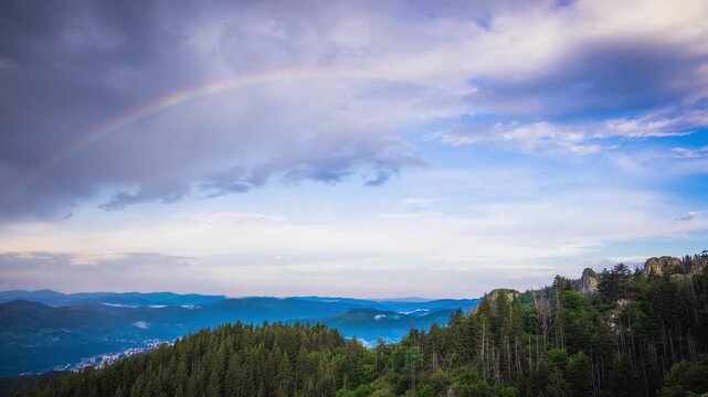Multi-colored rainbow flaunts on top of the Rhodope Mountains above intermountain valley with the village of Smolyan